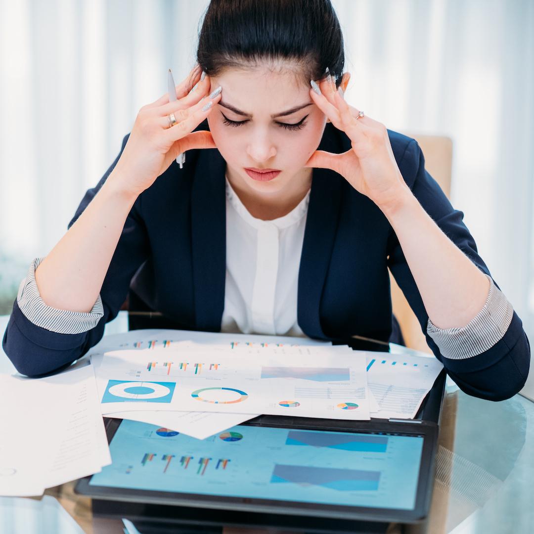 Woman at work holding her head while looking at documents and a tablet
